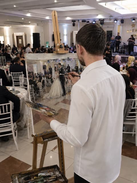 Ressam, düğün salonunda şövalesinin başında gelin ve damadı tuvale çiziyor