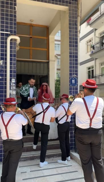 Kırmızı şapkalı bando ekibi, gelin ve damadın çıkışında apartman önünde çalıyor